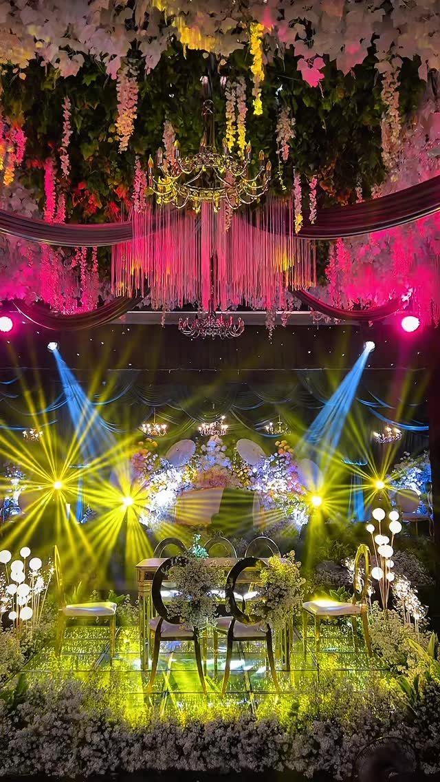 7 Wedding Stage Decorations for Romantic Receptions 5 Wedding stage with hanging floral installations, chandeliers, and dramatic colorful spotlights.