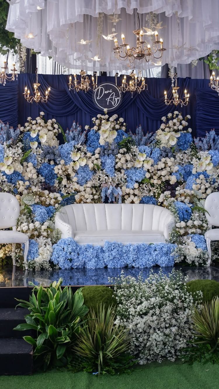 7 Wedding Stage Decorations for Romantic Receptions 7 Wedding stage with white sofa, blue and white floral wall, and gold chandeliers.