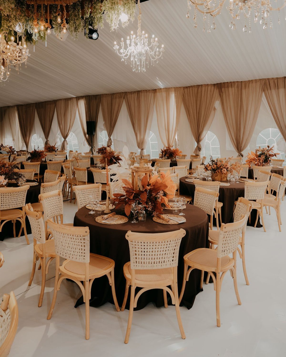 Wedding reception tables with dark brown cloths and autumn floral centerpieces under chandeliers.