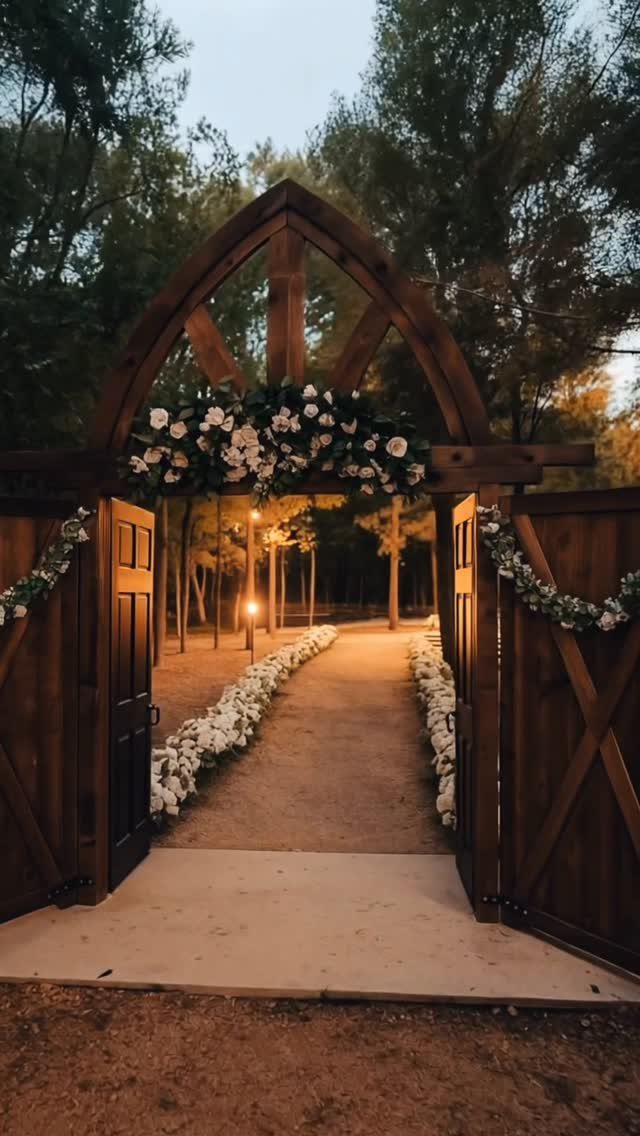 Wooden arched gateway opening to a flower-lined path in a rustic outdoor forest setting