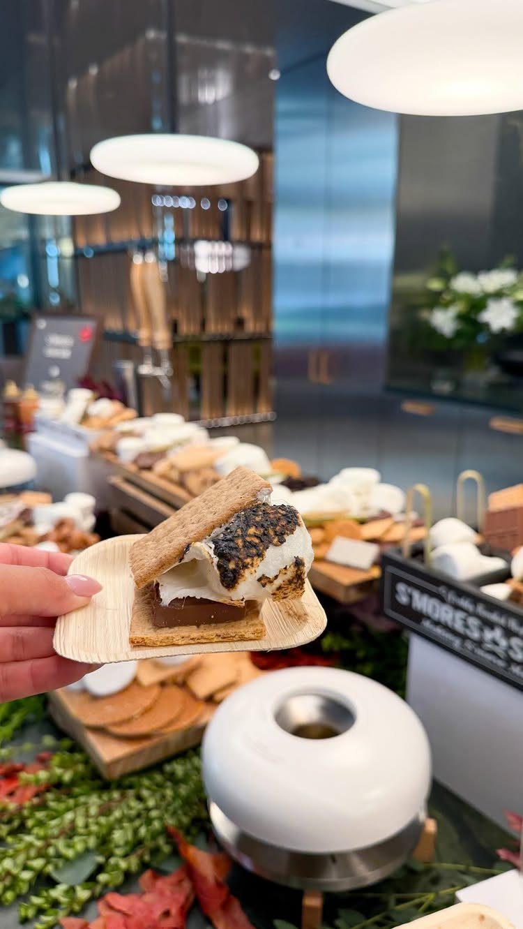 S'more with toasted marshmallow on a wooden board at a s'mores station buffet.