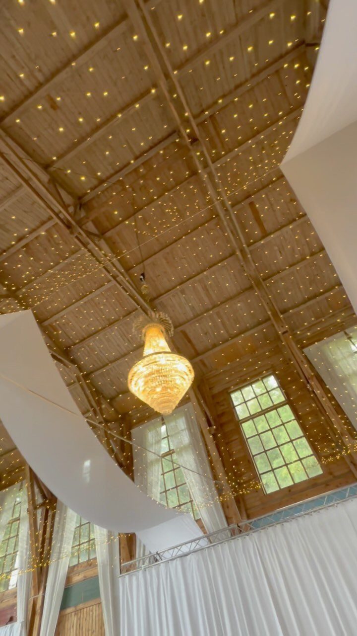 Wooden ceiling with warm string lights and a large crystal chandelier in a venue