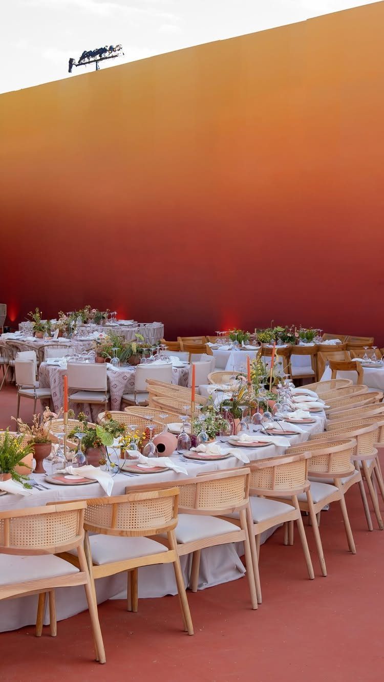 Wedding dining table with light wood chairs against a terracotta gradient wall.