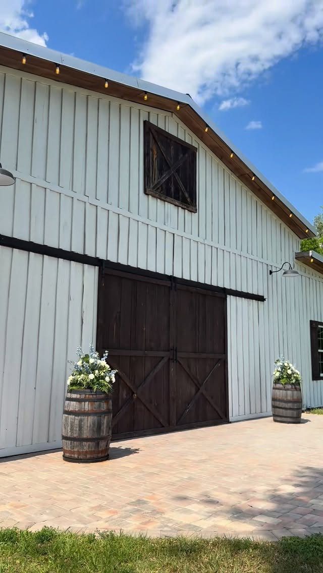White wooden barn with dark brown sliding doors and flower barrels on patio
