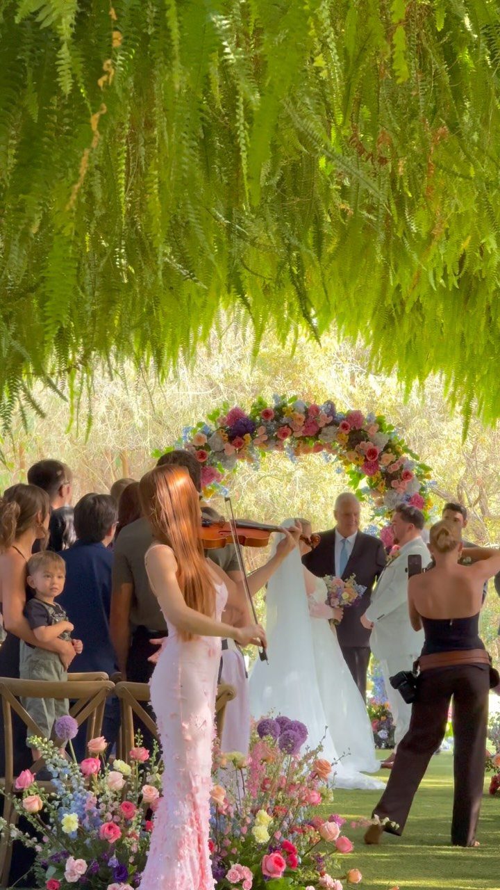 10 Wedding Venue Decorations for a Standout Celebration 7 Wedding ceremony with a floral arch, bride and groom, and a violinist.