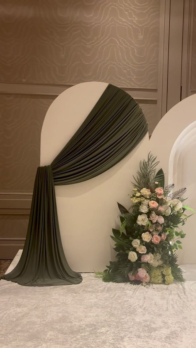 10 Wedding Venue Decorations for a Standout Celebration 8 White circular ceremony backdrop with olive green fabric drape and floral arrangement.