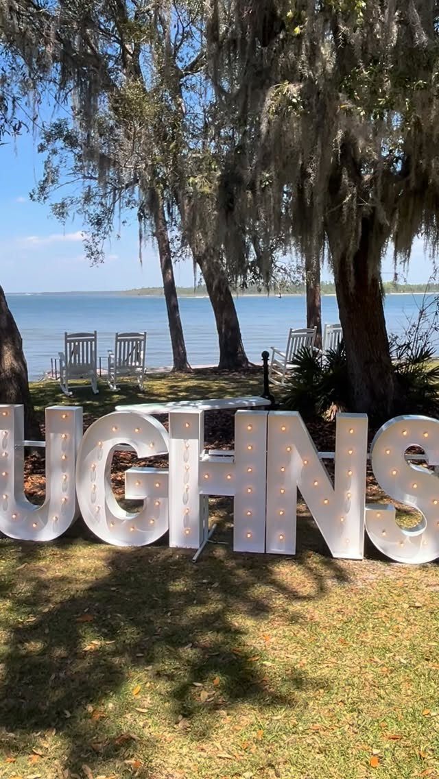 10 Wedding Venue Decorations for a Standout Celebration 9 Large white marquee light letters standing on grass with trees and water behind.