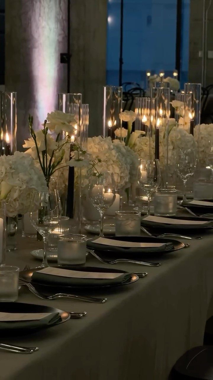 10 Wedding Venue Decorations for a Standout Celebration 2 Elegant wedding table settings with white flowers, black plates, and glowing cylinder candles.