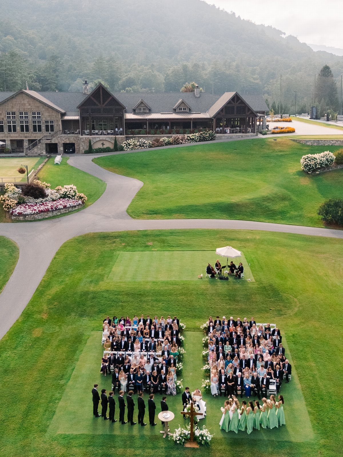 Wedding Venues Western Couples Love: 16 Ideas 3 Outdoor wedding ceremony on a green lawn with a large lodge and mountains.