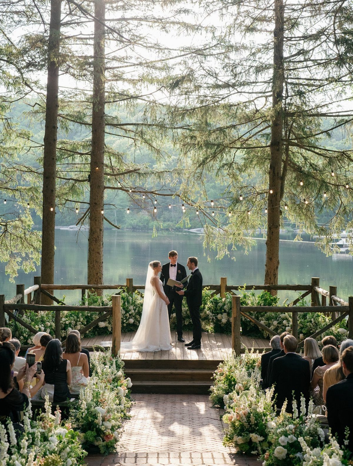 Wedding Venues Western Couples Love: 16 Ideas 9 Wedding ceremony on a wooden platform framed by tall pine trees overlooking a lake.