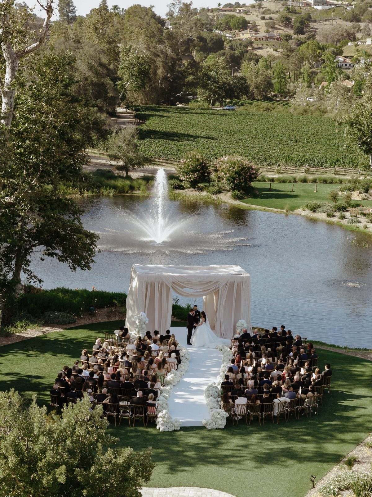 Wedding Venues Western Couples Love: 16 Ideas 12 Wedding ceremony with a white canopy and aisle beside a pond with a fountain.