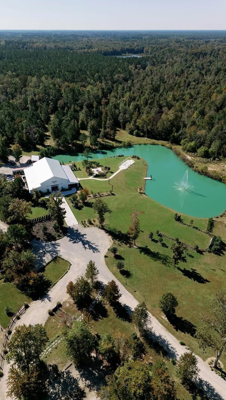 Wedding Venues Western Couples Love: 16 Ideas 1 White barn and turquoise pond surrounded by green forests and lawns in aerial view.