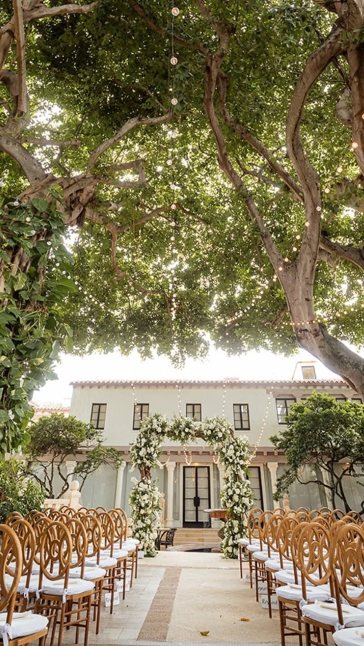 Wedding Venues Western Couples Love: 16 Ideas 16 Outdoor wedding ceremony setup with wooden chairs and a floral arch under a large tree.