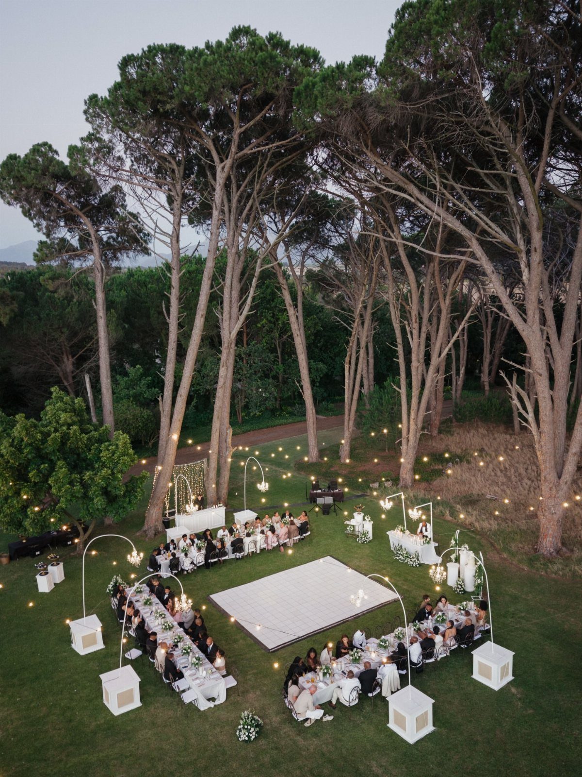 Wedding Venues Western Couples Love: 16 Ideas 10 Outdoor wedding reception with long white tables and a dance floor under tall trees.