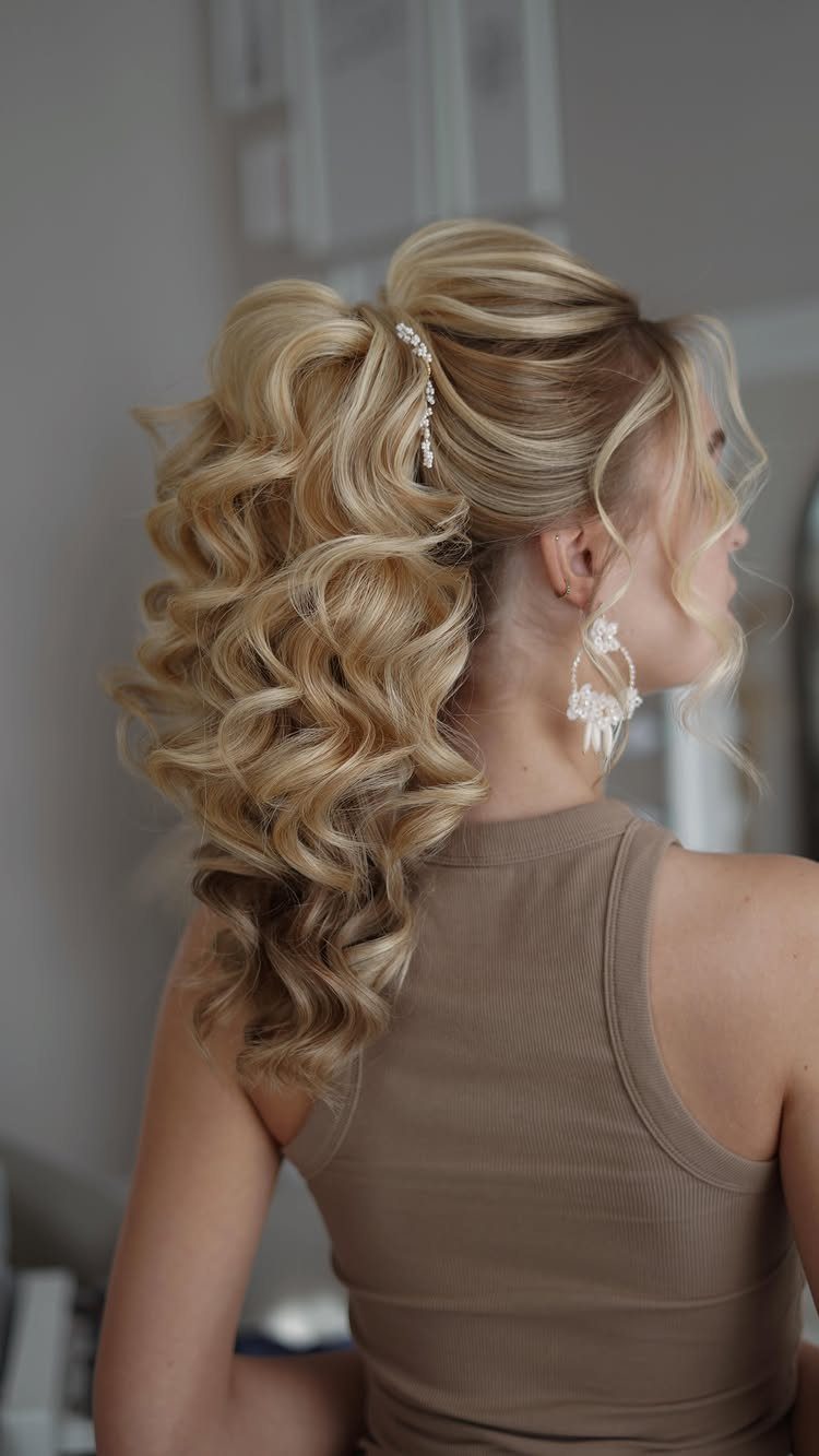 Blonde woman with voluminous curly half-up wedding hairstyle and decorative hair clip.