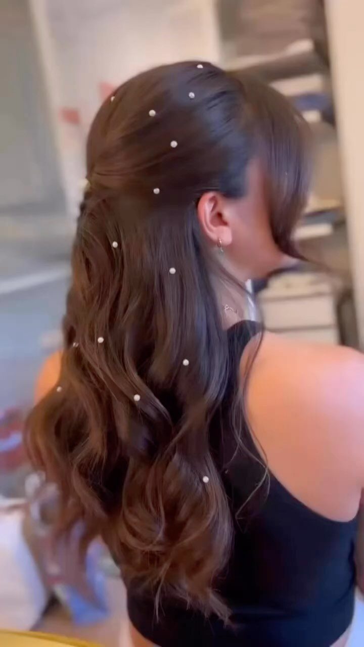 Woman with wavy brown hair in a half-updo decorated with small white pearls.