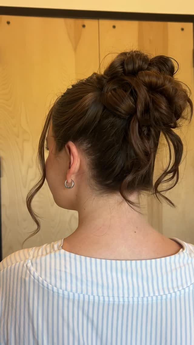 Woman with brown hair styled in a textured high bun with loose curls.