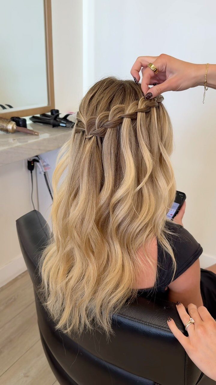 Blonde wavy hair with a waterfall braid being styled in a salon chair.